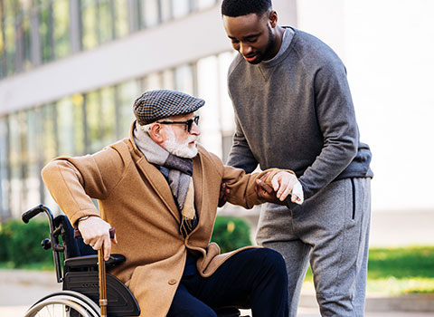 AdobeStock_231168548 Young man helps a senior man out of a wheelchair