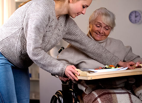 Young woman handing food tray to senior woman