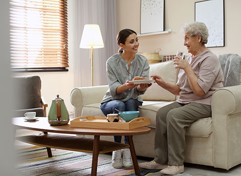 Young woman handing plate of food to smiling senior woman