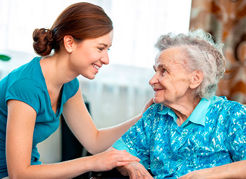 AdobeStock_44407430 Young female caregiver smiles at an elderly female woman